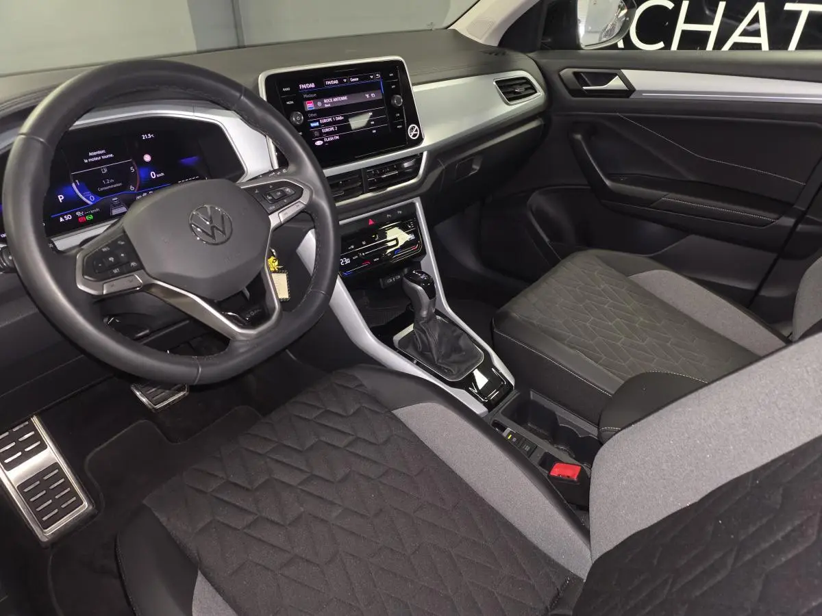 Intérieur avant du Volkswagen T-Roc 2025, sièges tissu noir/gris, tableau de bord gris étain avec écran tactile 8 pouces.
