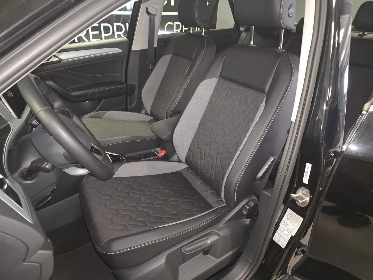 Vue intérieure côté conducteur du Volkswagen T-Roc noir, mettant en valeur les sièges tissu noir et gris avec coutures apparentes.