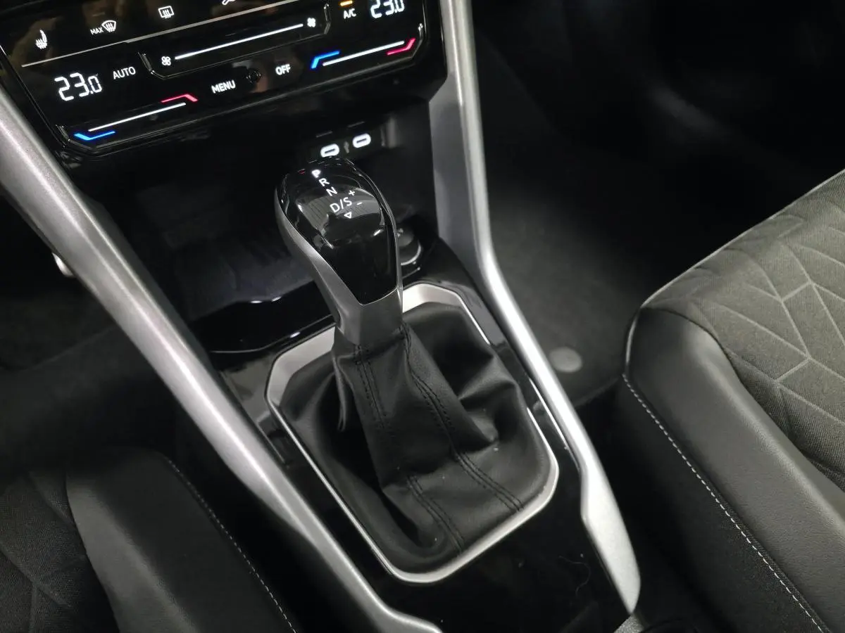 Gros plan sur la console centrale noire du Volkswagen T-Roc 2025 avec levier de vitesse automatique et sièges tissu gris.