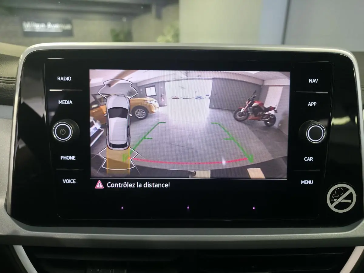 Écran tactile intérieur montrant la caméra de recul avec vue arrière et alertes de distance du Volkswagen T-Roc noir.