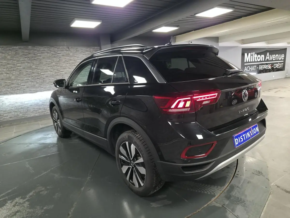 Volkswagen T-Roc noir en 3/4 arrière droit, avec feux LED allumés et jantes alliage distinctives.