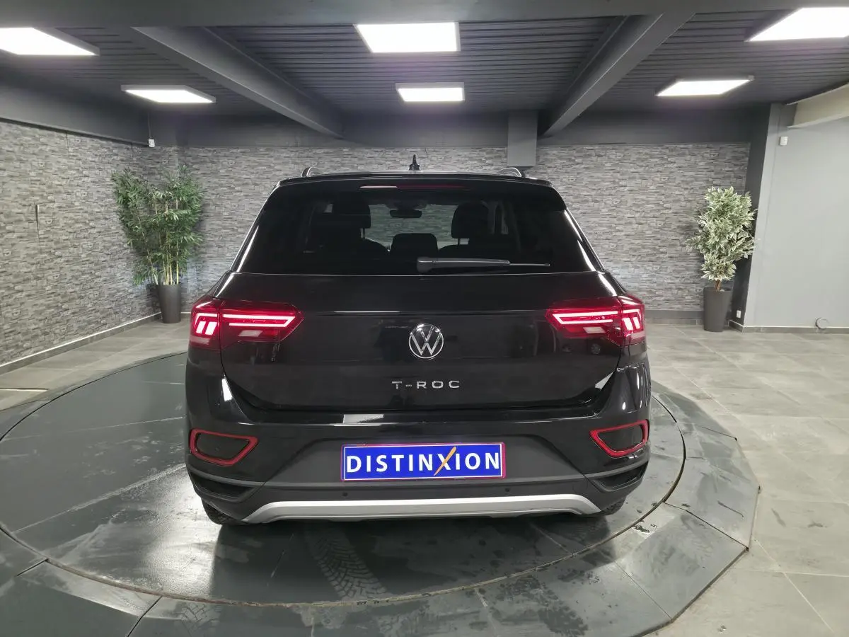 Vue arrière d'un Volkswagen T-Roc noir 2025 avec feux LED allumés dans un showroom intérieur.