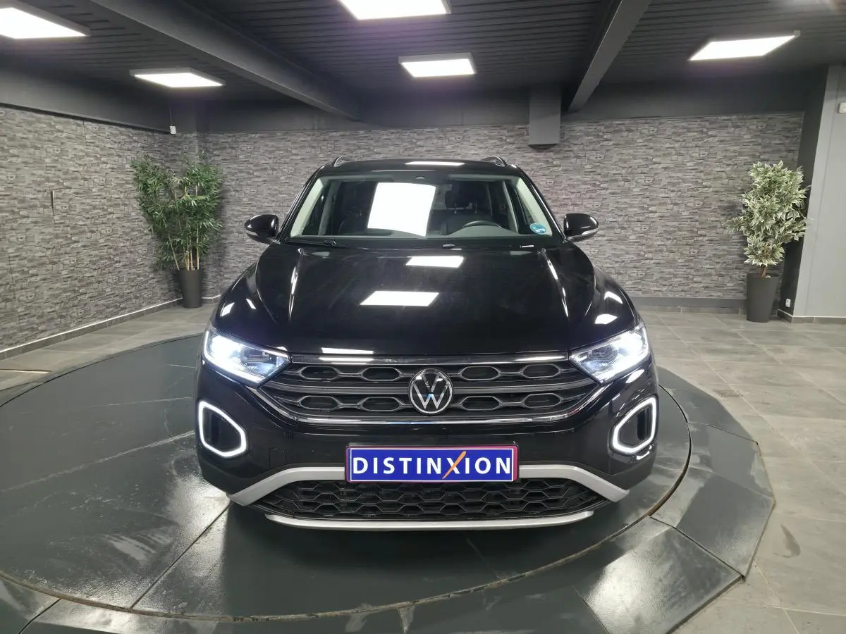 Vue frontale d'un Volkswagen T-Roc noir avec éclairage LED allumé dans un showroom intérieur.