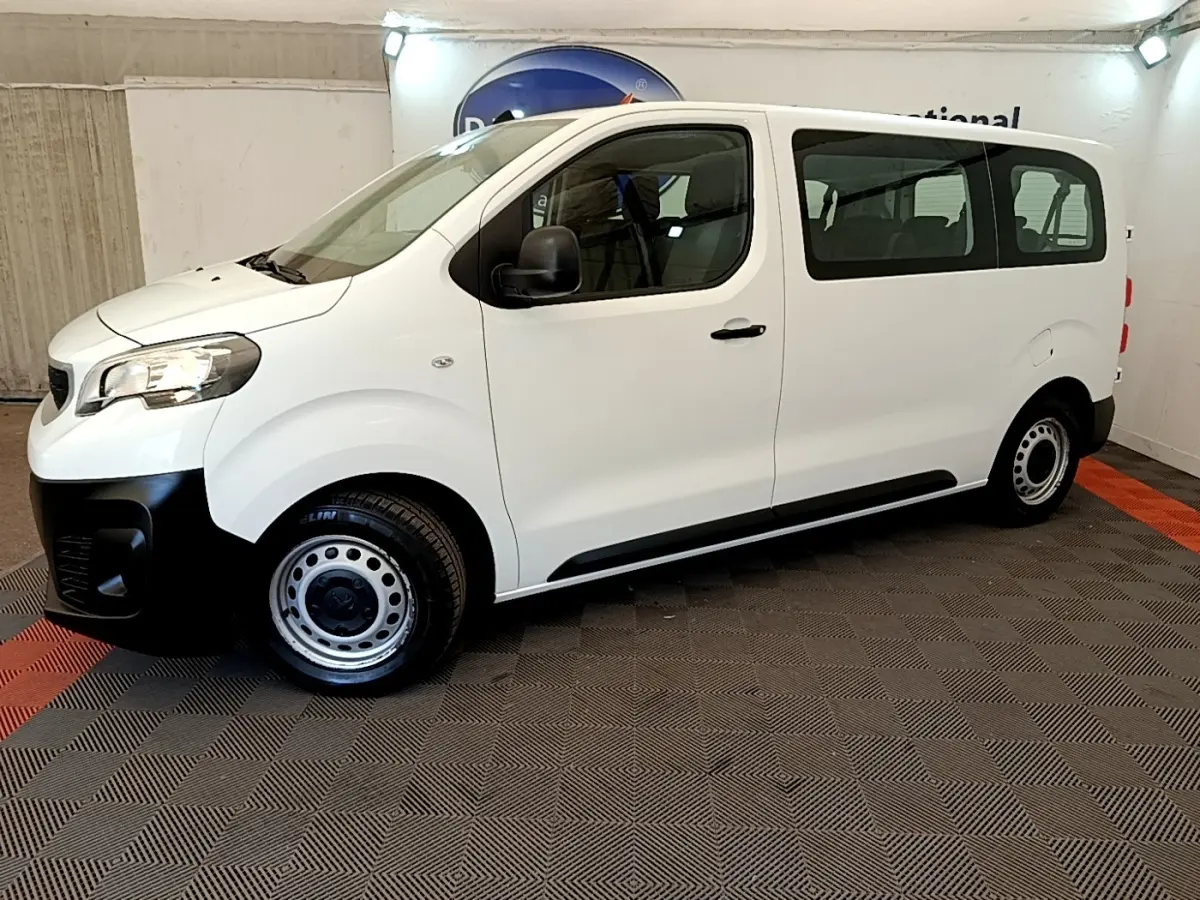 Vue de profil côté gauche d’un Peugeot Traveller blanc 2018 avec jantes acier et pare-chocs noirs, en intérieur.