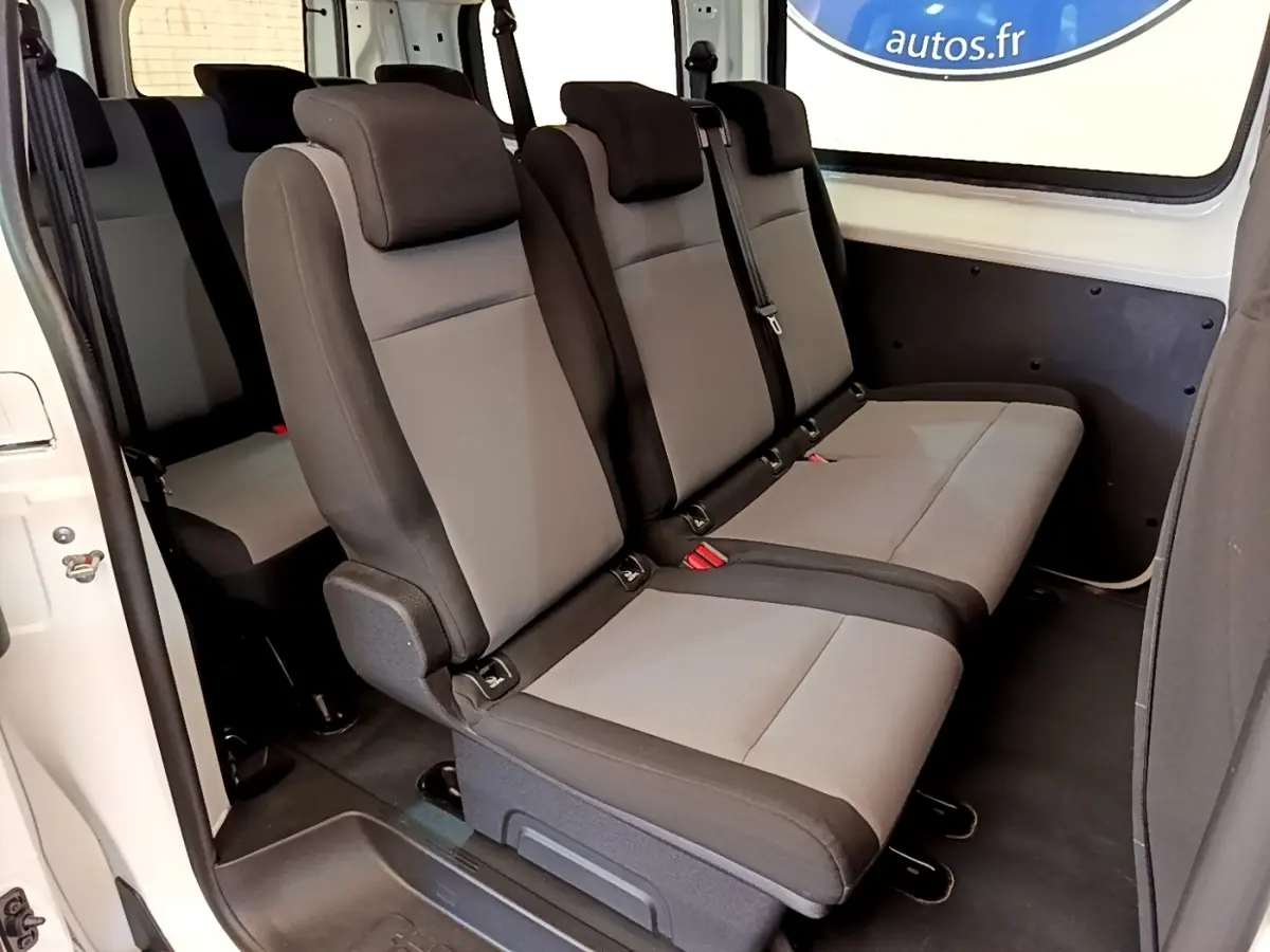 Vue intérieure latérale droite des sièges gris et noirs du Peugeot Traveller blanc de 2018 avec porte coulissante ouverte.