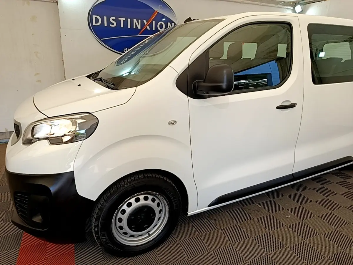 Vue de profil côté gauche d’un Peugeot Traveller blanc 2018 avec pare-chocs avant noir et jantes acier.