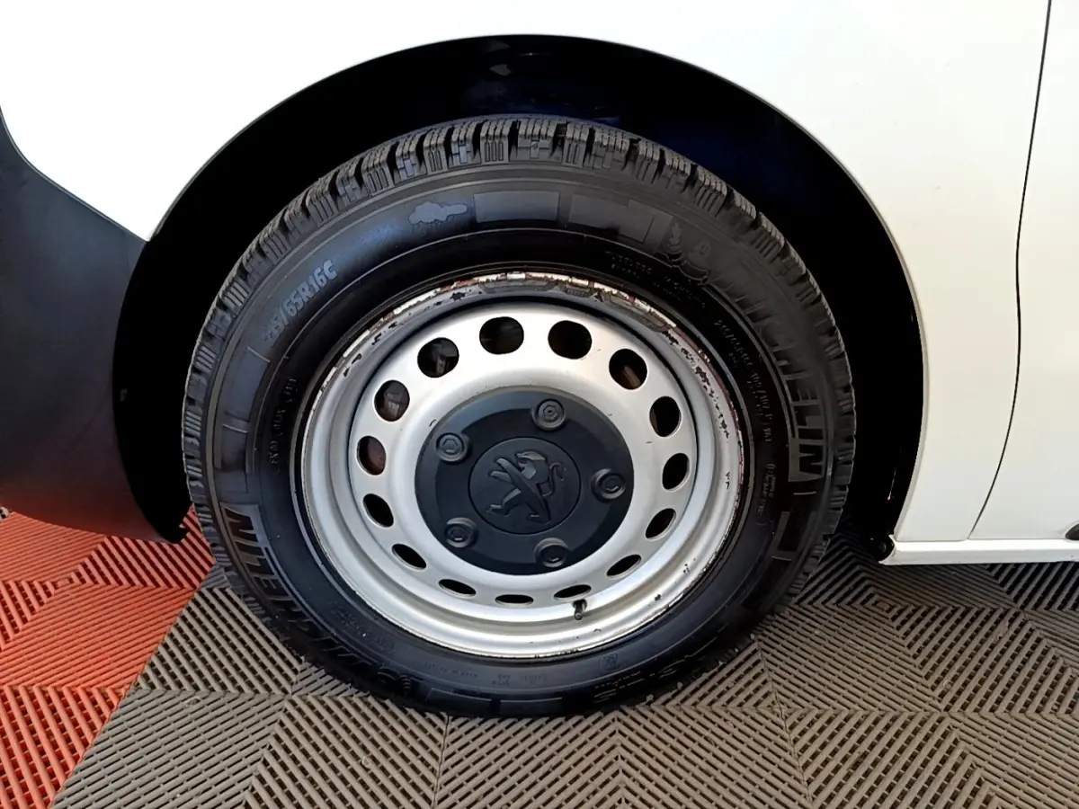 Gros plan sur la roue avant gauche d’un Peugeot Traveller blanc de 2018 avec jante acier et logo Peugeot central.