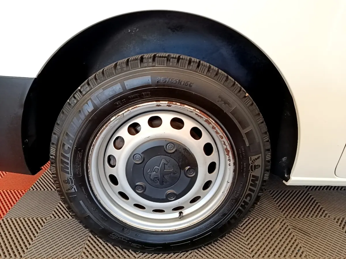 Gros plan sur la roue arrière droite d’un Peugeot Traveller blanc de 2018, avec jante acier et traces de rouille.