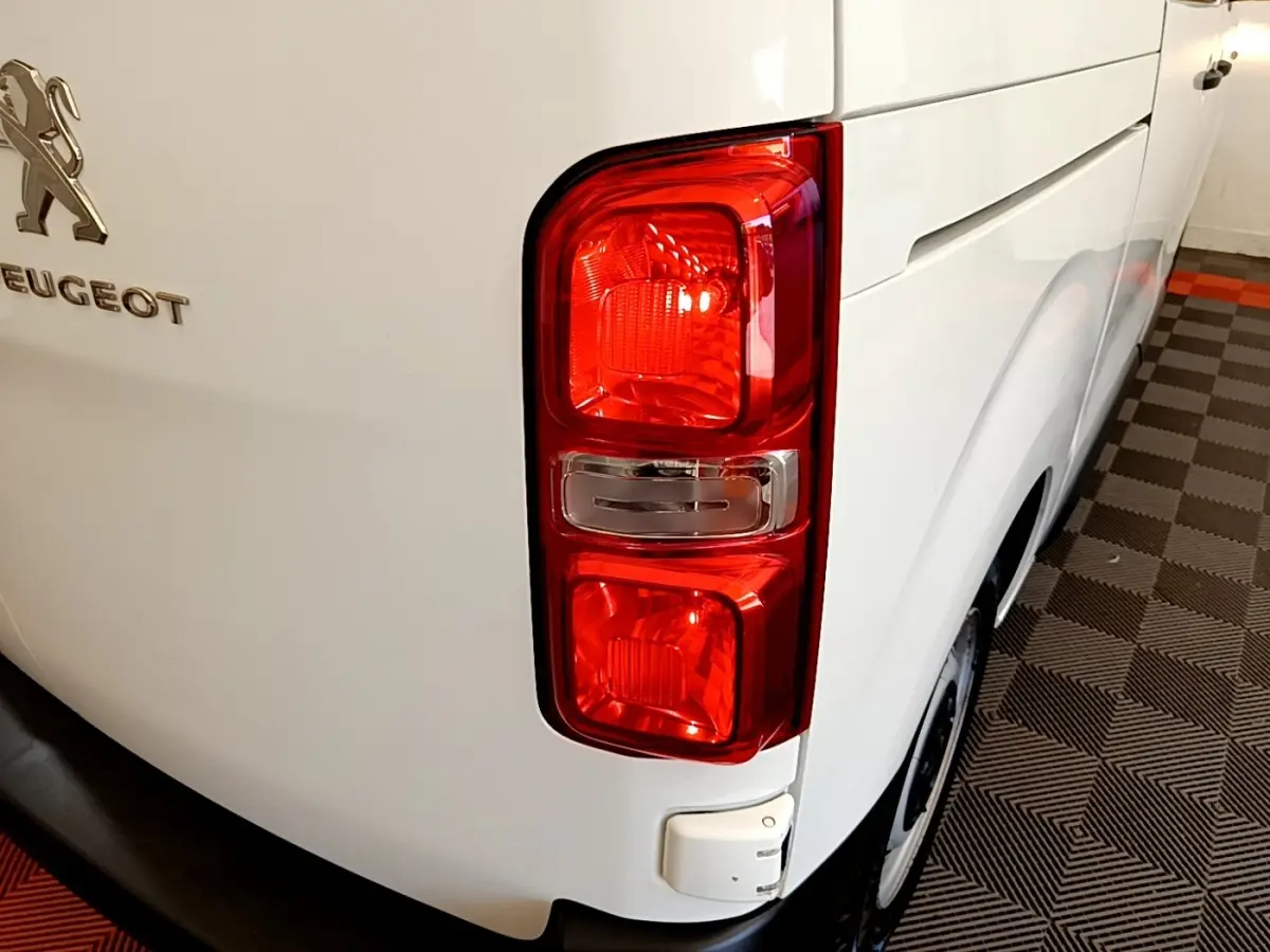 Gros plan sur le feu arrière droit d’un Peugeot Traveller blanc de 2018, avec logo et partie latérale visible.