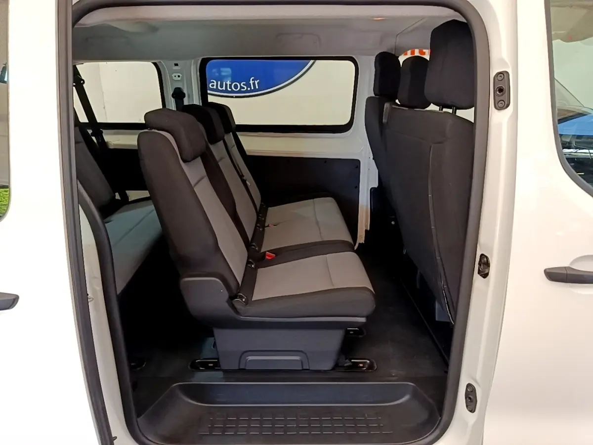 Vue latérale intérieure du Peugeot Traveller blanc 2018 montrant la rangée de sièges en tissu gris et noir.