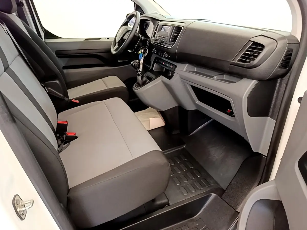 Vue intérieure côté conducteur du Peugeot Traveller 2018 blanc, montrant sièges gris et tableau de bord avec boîte manuelle.