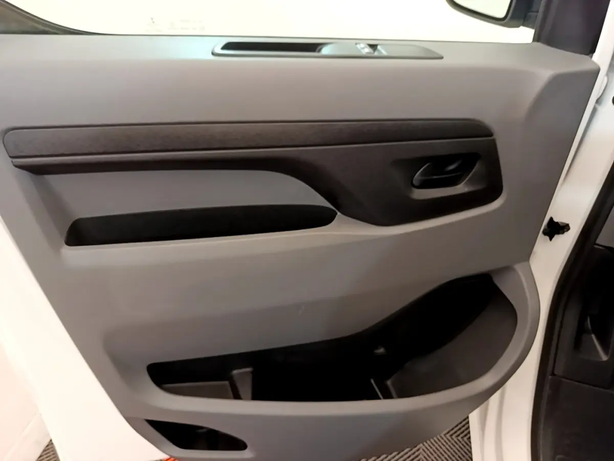 Vue intérieure du panneau de porte avant gauche du Peugeot Traveller blanc, avec poignée noire et rangements intégrés.
