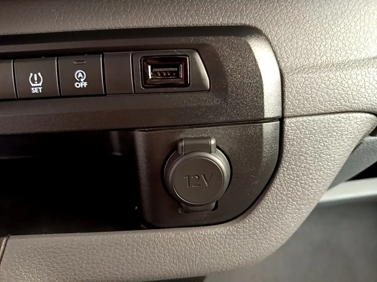 Gros plan sur la console centrale noire du Peugeot Traveller 2018, montrant prise 12V, port USB et boutons de contrôle.