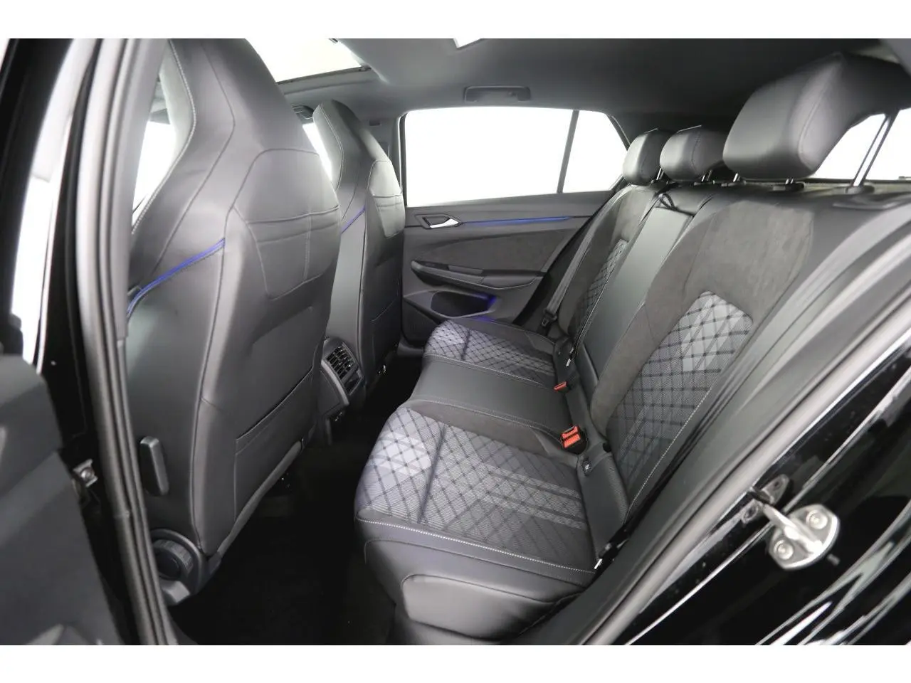 Vue côté droit de l’arrière intérieur de la Volkswagen Golf VIII avec sièges en tissu et cuir noir à motifs géométriques.