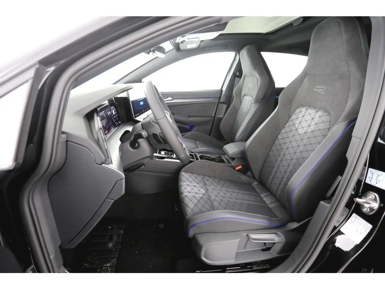 Vue intérieure côté conducteur de la Volkswagen Golf VIII R-Line avec sièges sport gris à surpiqûres bleues et tableau de bord digital.