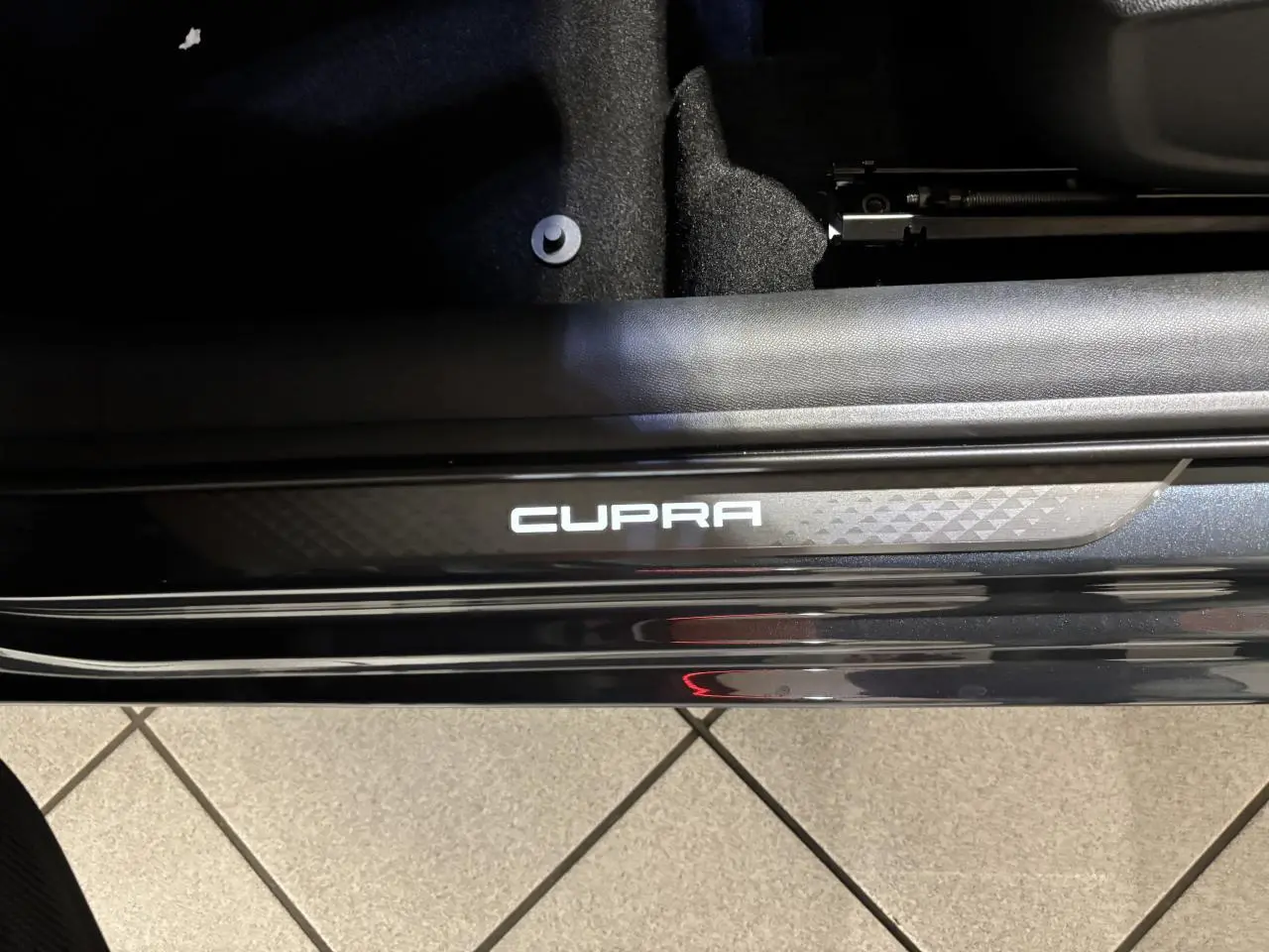 Gros plan sur le seuil de porte noir brillant avec logo CUPRA blanc, intérieur suédine noire visible en arrière-plan.