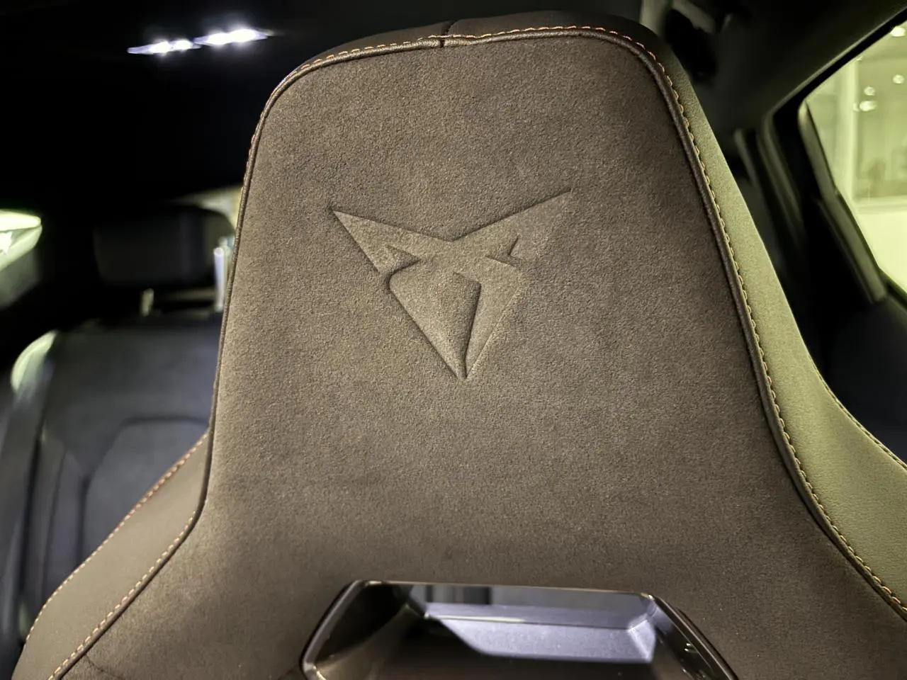 Gros plan sur le dossier avant en suédine noire avec logo Cupra embossé et surpiqûres cuivrées dans l’habitacle.