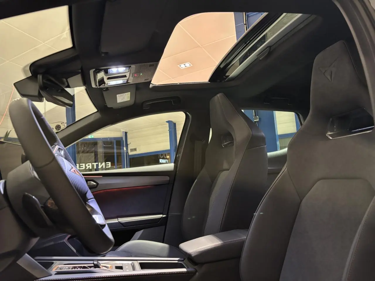 Intérieur CUPRA Leon 2026 vu côté gauche, sièges baquets noirs et toit ouvrant panoramique visible.