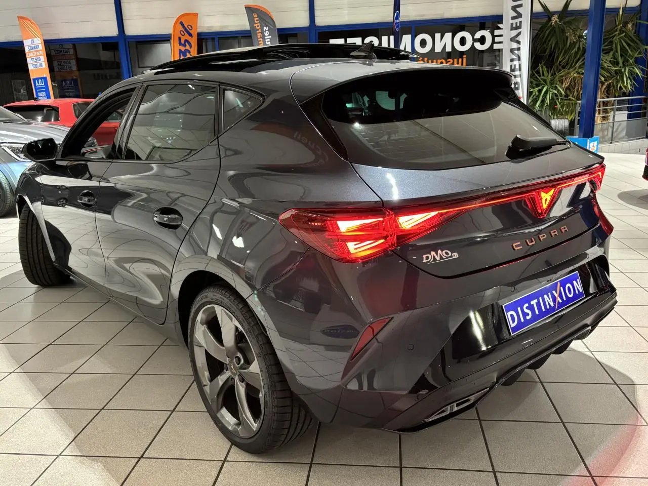 Vue 3/4 arrière droite d'une CUPRA Leon gris Graphène avec feux arrière allumés et jantes alliage 5 branches.