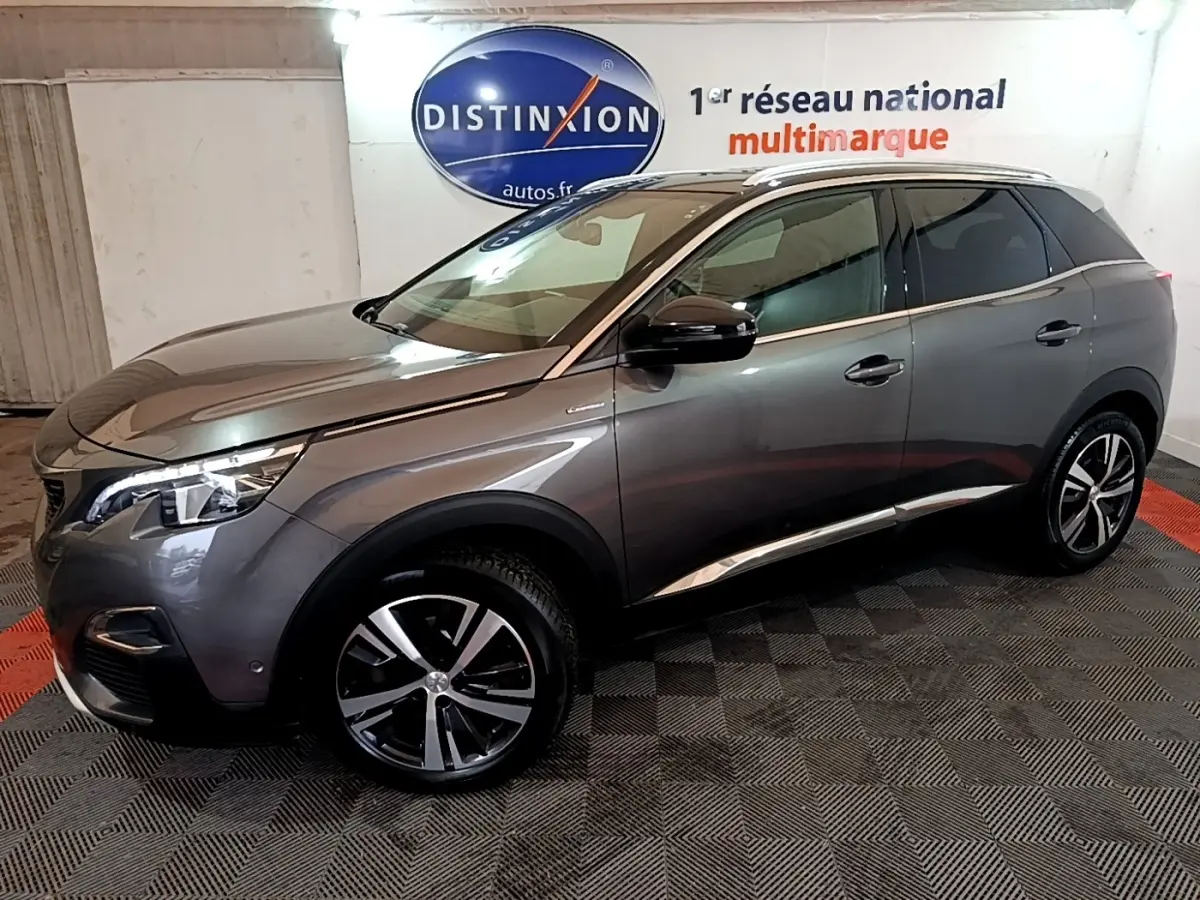 Peugeot 3008 gris foncé en vue 3/4 avant droit, avec jantes alliage et feux LED allumés, stationné en intérieur.