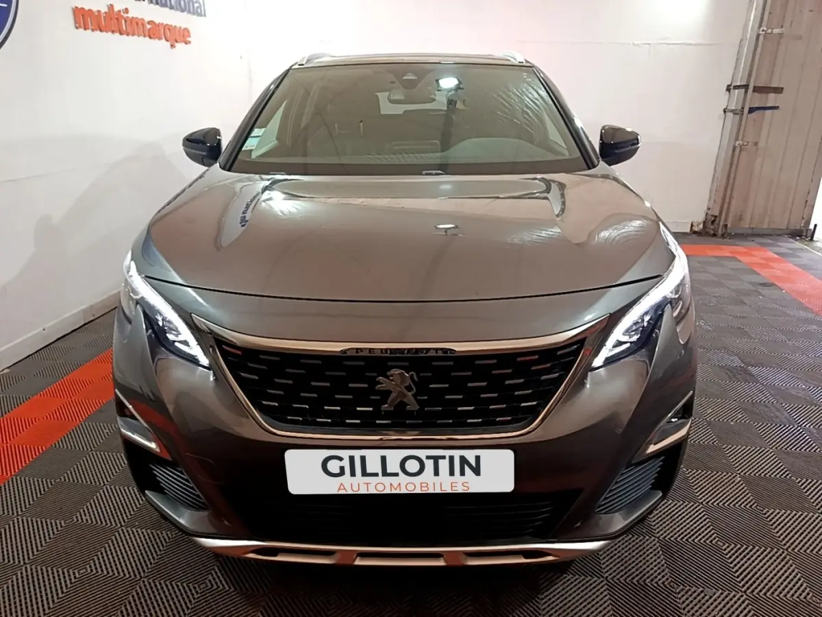 Vue avant d'un Peugeot 3008 gris foncé avec calandre noire et phares LED allumés dans un showroom.