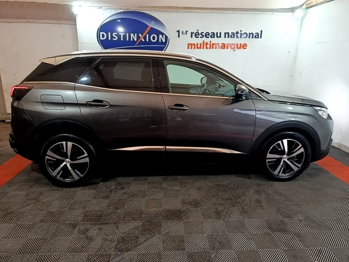 Profil droit d'un Peugeot 3008 gris foncé GT Line 2020 avec jantes alliage et toit noir dans un showroom.