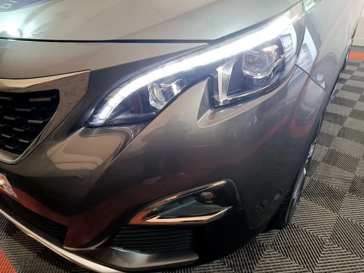 Gros plan sur l'avant droit gris foncé du Peugeot 3008, mettant en valeur le phare LED et la calandre distinctive.