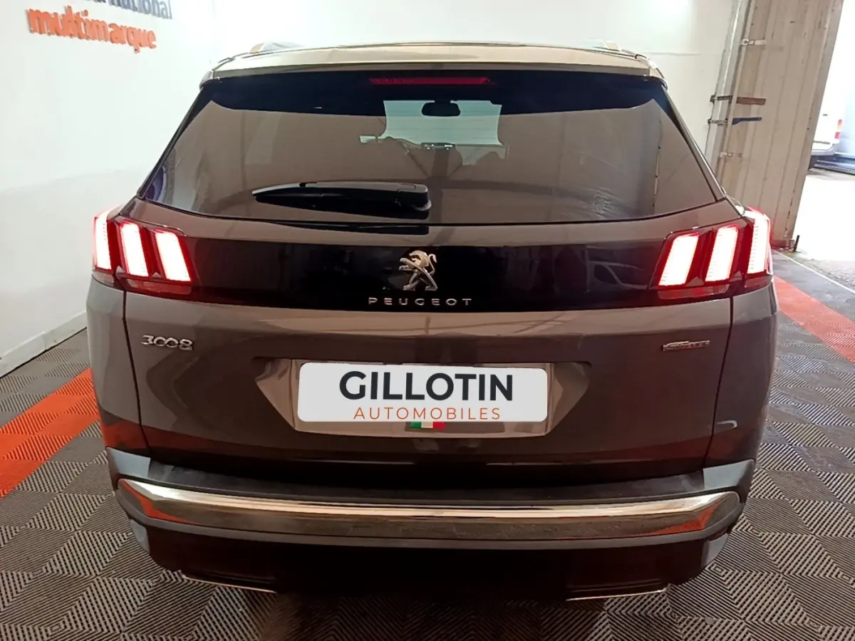 Vue arrière d'un Peugeot 3008 gris foncé avec feux LED allumés et logo Peugeot visible sur hayon noir brillant.