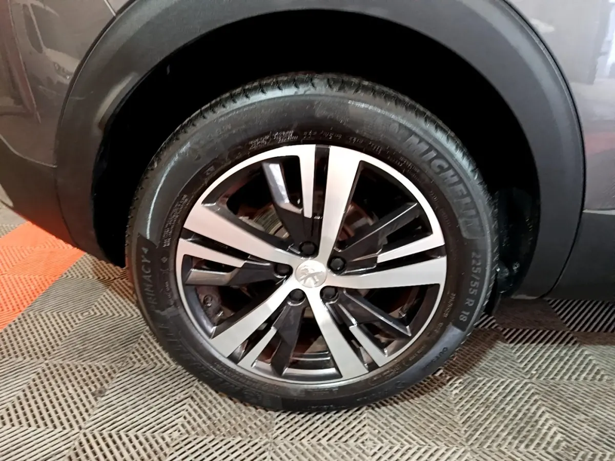 Gros plan sur la roue avant droite du Peugeot 3008 gris foncé, mettant en valeur la jante alliage bicolore.