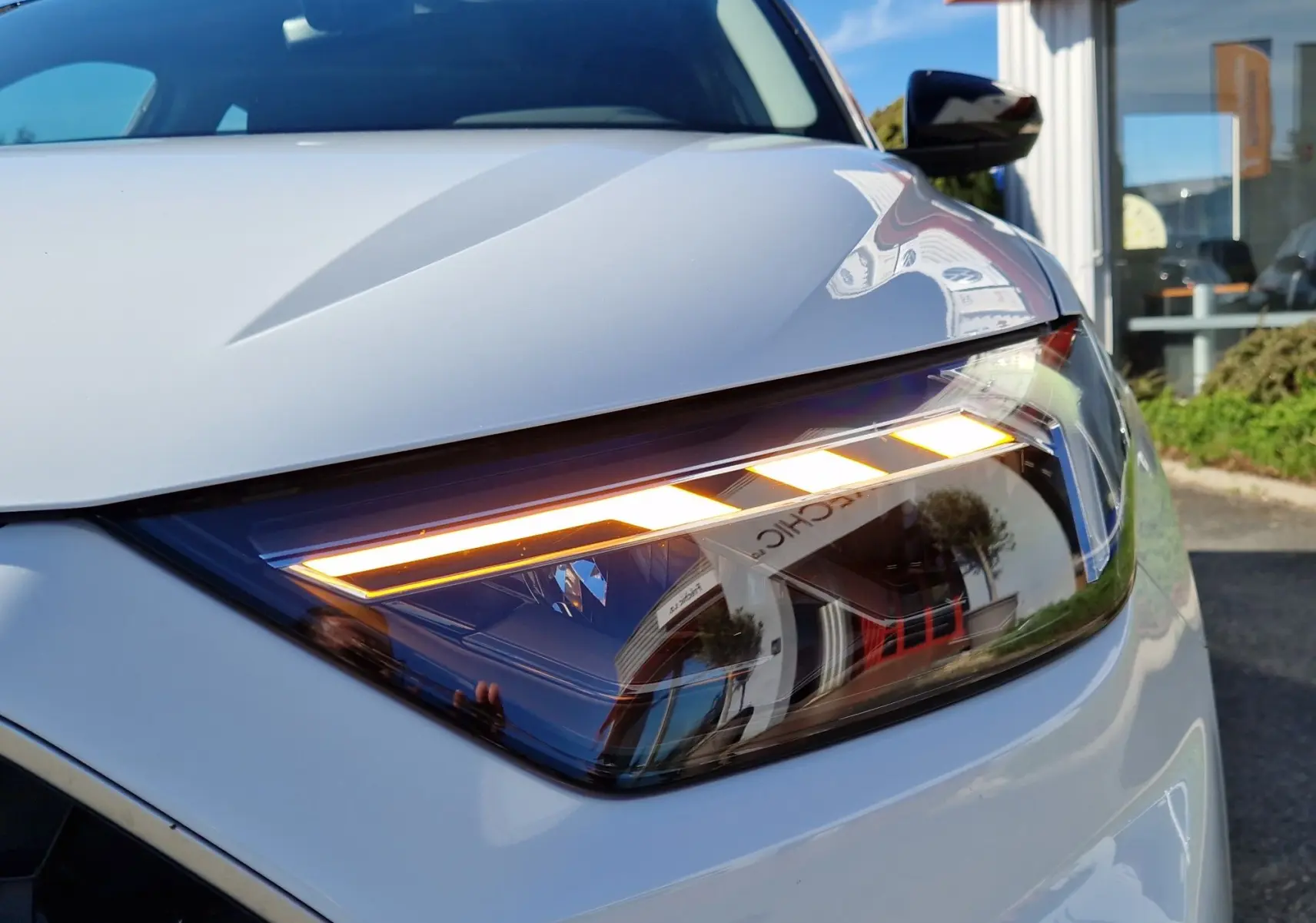 Gros plan sur le phare avant droit allumé de l'Audi A1 Sportback blanc glacier, soulignant ses lignes modernes et précises.