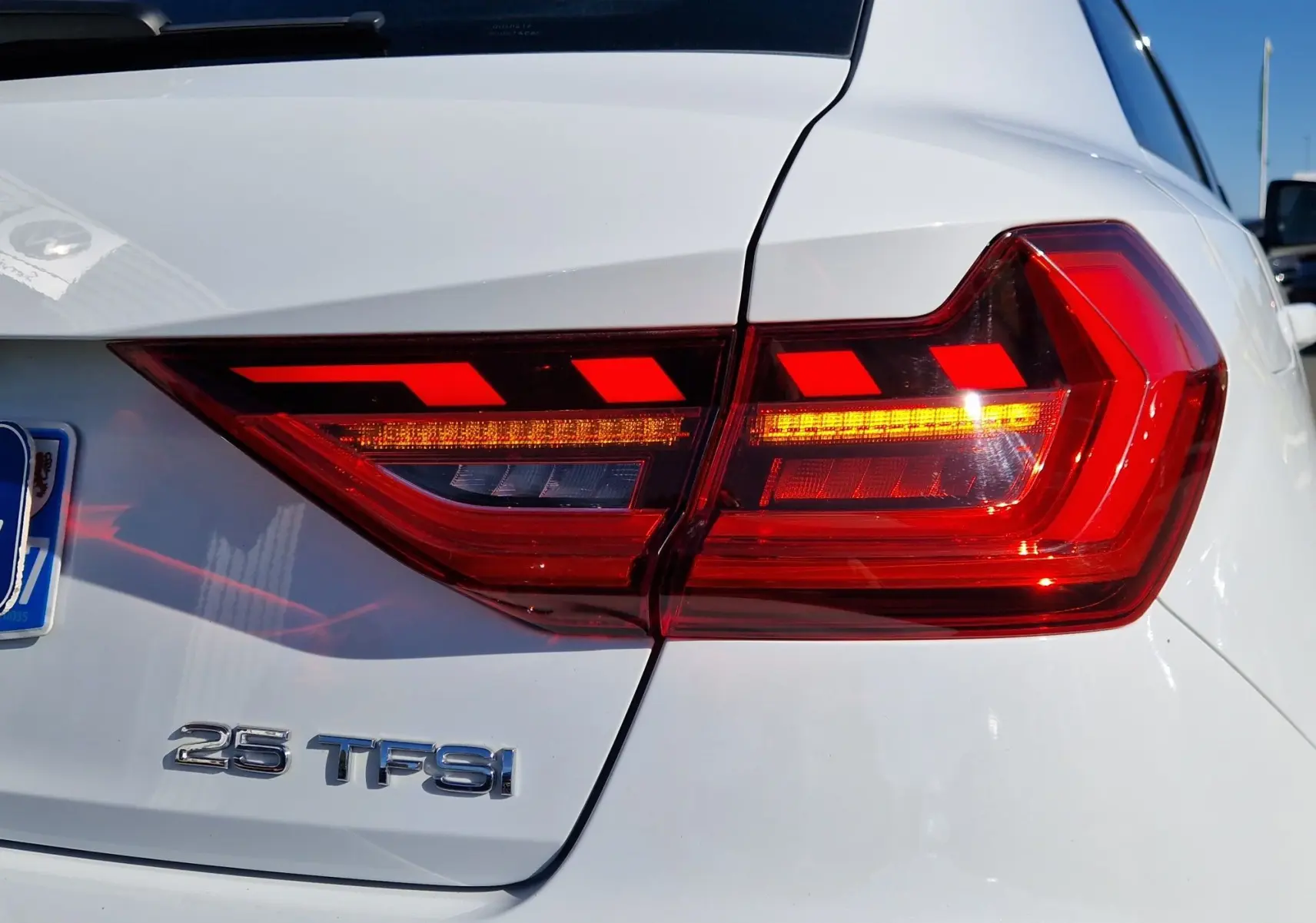 Gros plan sur le feu arrière droit rouge vif et l’inscription 25 TFSI sur la carrosserie blanche glacier d’une Audi A1 Sportback.