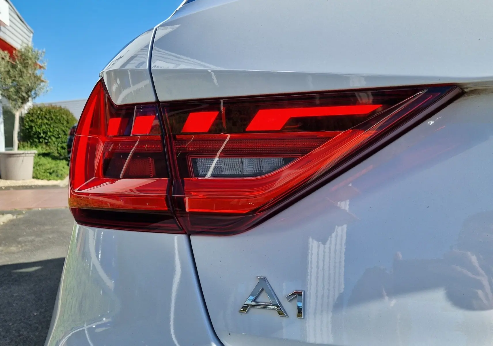 Gros plan sur le feu arrière droit rouge vif d’une Audi A1 Sportback blanc glacier avec le logo A1 visible sur le hayon.