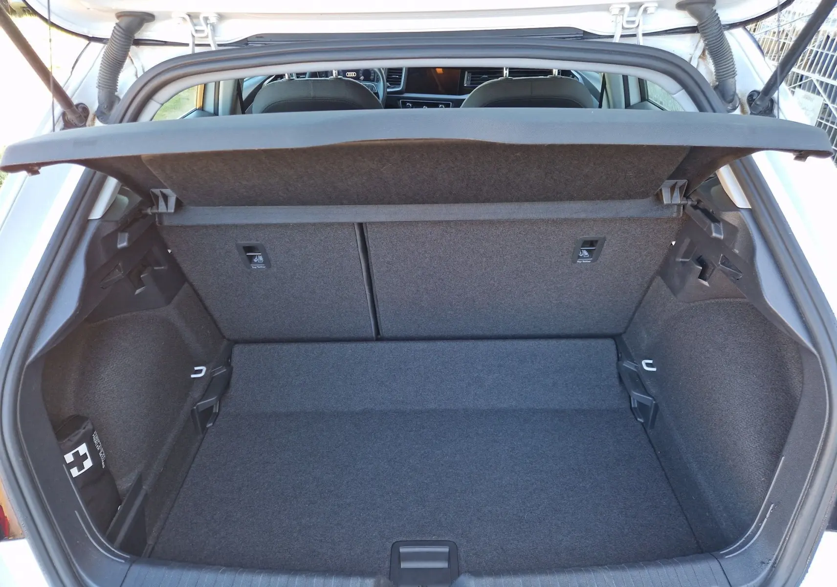 Vue intérieure du coffre ouvert d'une Audi A1 Sportback blanc glacier, montrant l'espace de rangement et la tablette arrière.