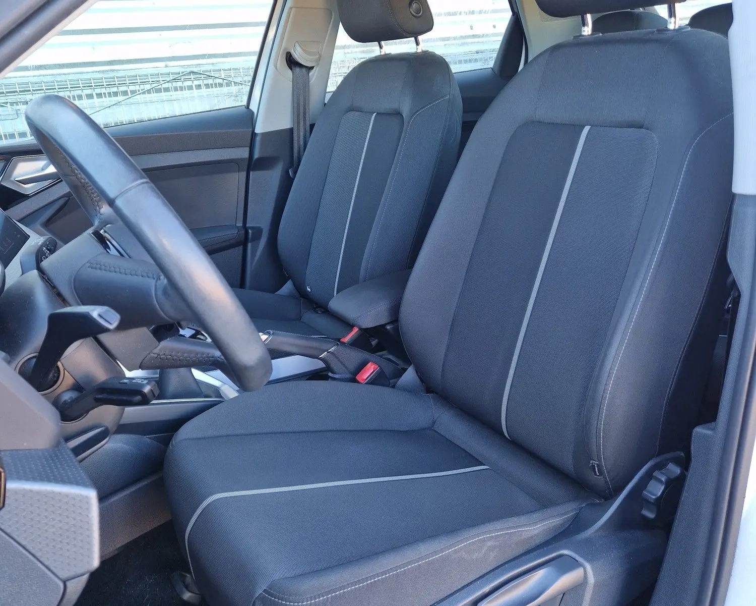 Vue intérieure côté conducteur de l'Audi A1 Sportback blanc glacier, mettant en valeur les sièges avant en tissu noir avec surpiqûres grises.