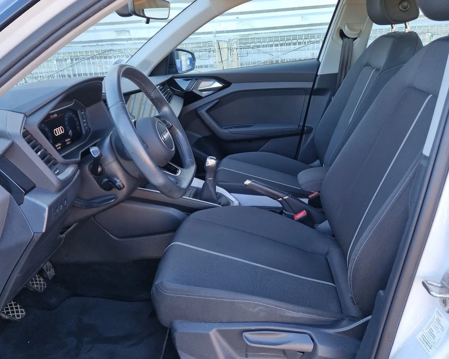 Vue intérieure côté conducteur de l'Audi A1 Sportback blanc glacier 2020 avec sièges noirs et volant multifonction.