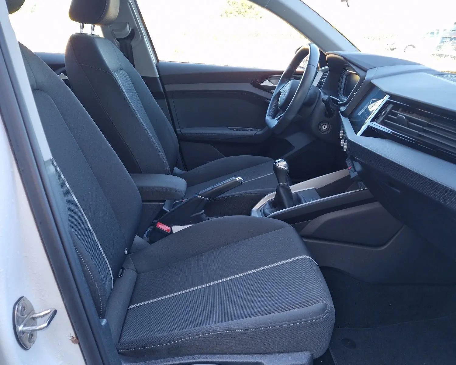 Vue intérieure côté gauche de l'Audi A1 Sportback blanc glacier 2020, montrant les sièges avant et la console centrale avec boîte manuelle.