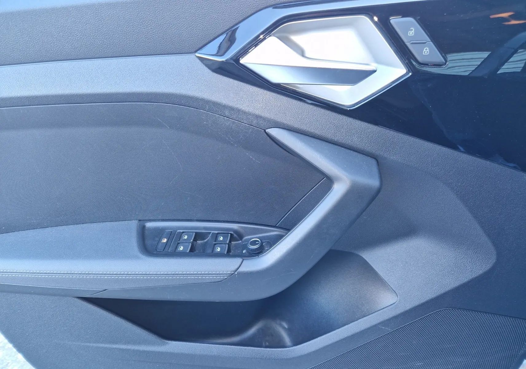 Détail de la porte côté conducteur noire de l'Audi A1 Sportback 25 TFSI 2020 avec commandes des vitres et poignée argentée.