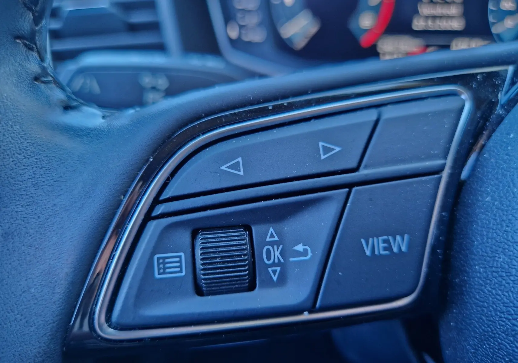 Gros plan sur les commandes multifonctions noires du volant d'un Audi A1 Sportback blanc glacier, avec boutons fléchés et "VIEW".