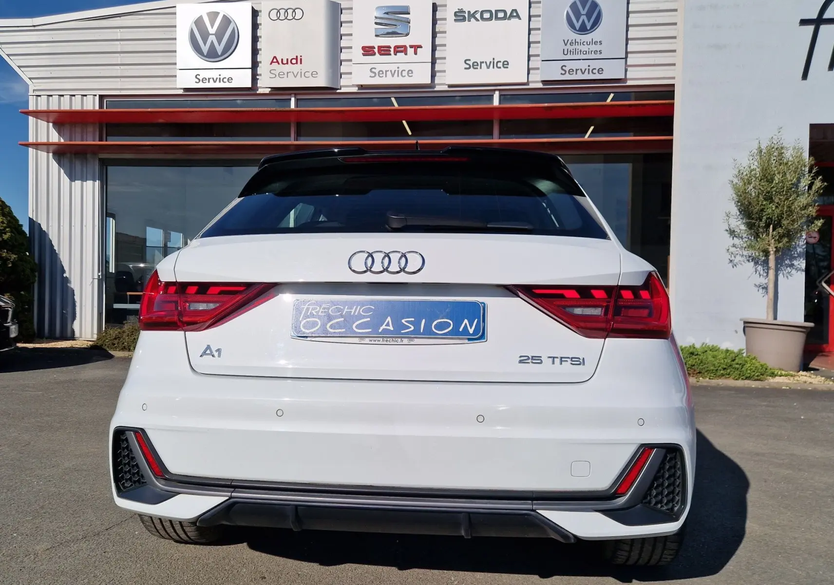 Vue arrière d'une Audi A1 Sportback blanc glacier 2020 avec feux LED et logo distinctif sur un parking de concession.