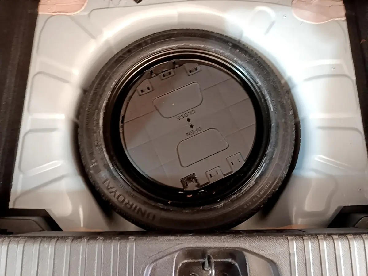 Vue plongeante sur la roue de secours noire dans le coffre blanc d'une Renault Clio Business Blue dCi 85 2020.