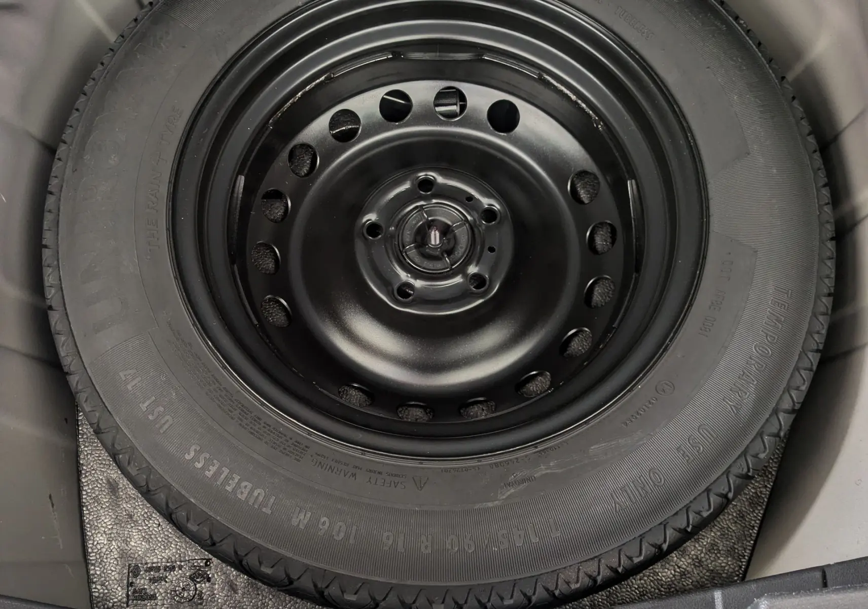 Roue de secours noire montée sur jante acier, vue en plongée dans le coffre d’un Nissan Juke rouge 2020.
