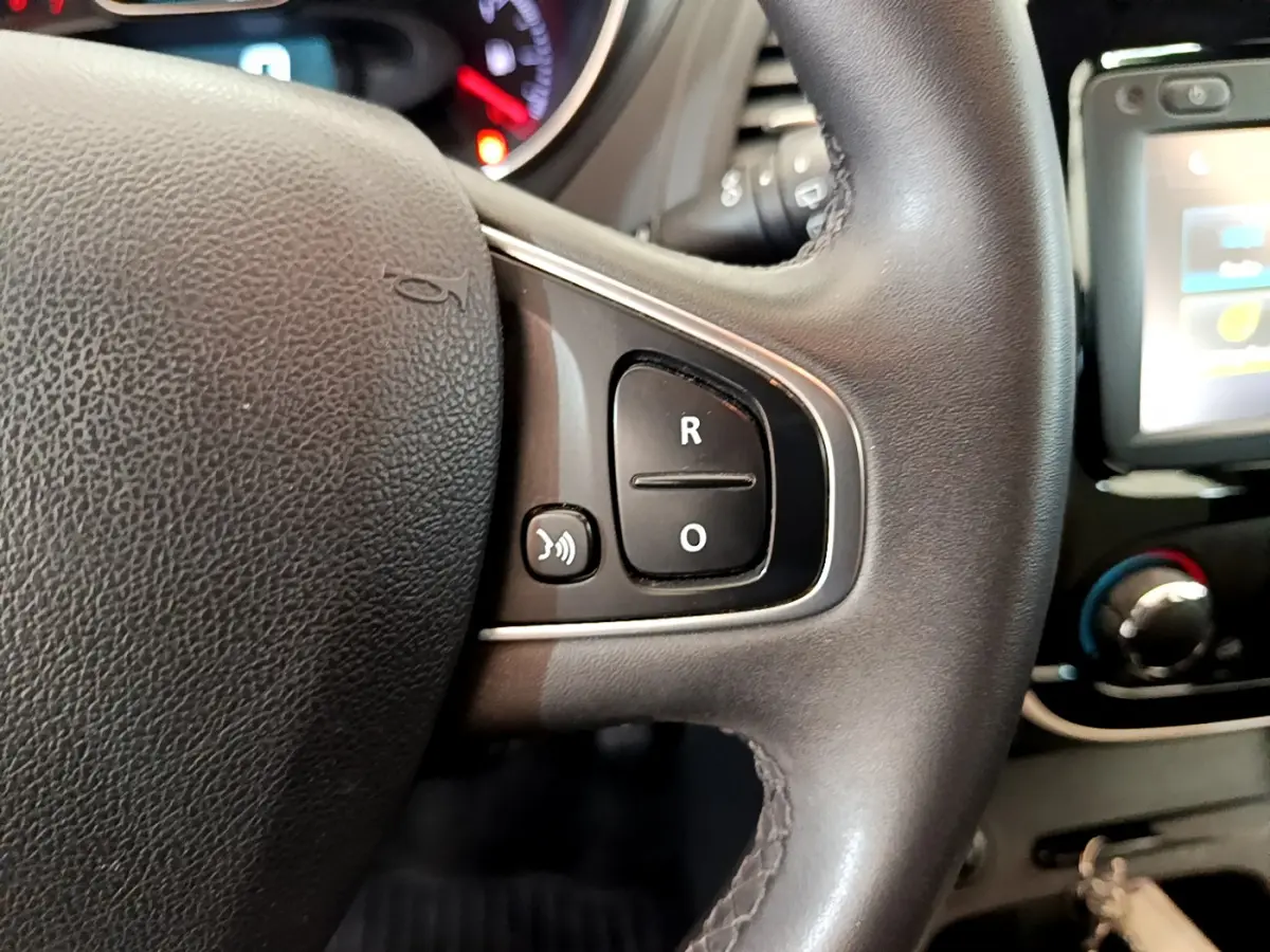 Gros plan sur le volant cuir du Renault Captur Business gris foncé, avec commandes vocales et écran tactile visible en arrière-plan.
