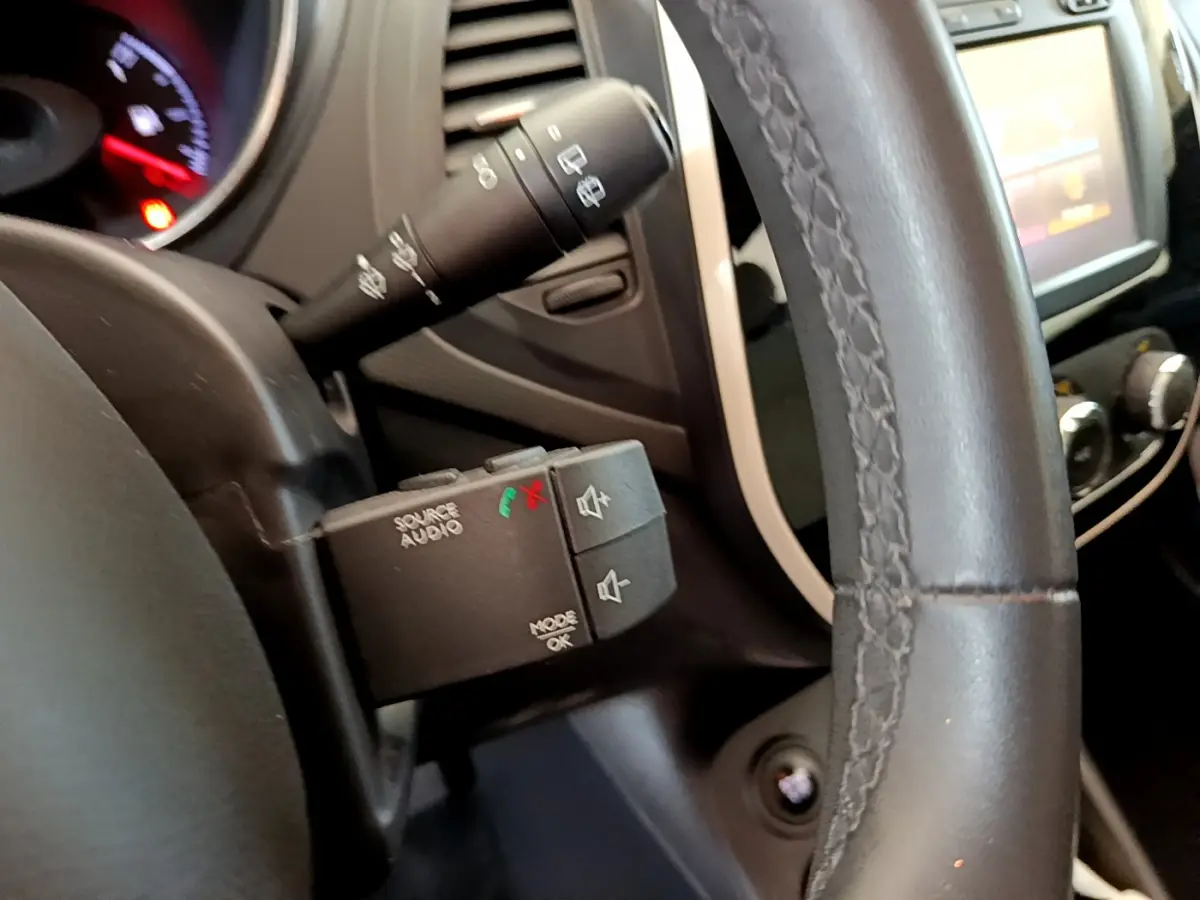 Gros plan sur la commande audio au volant cuir du Renault Captur gris foncé, avec tableau de bord et écran tactile en arrière-plan.