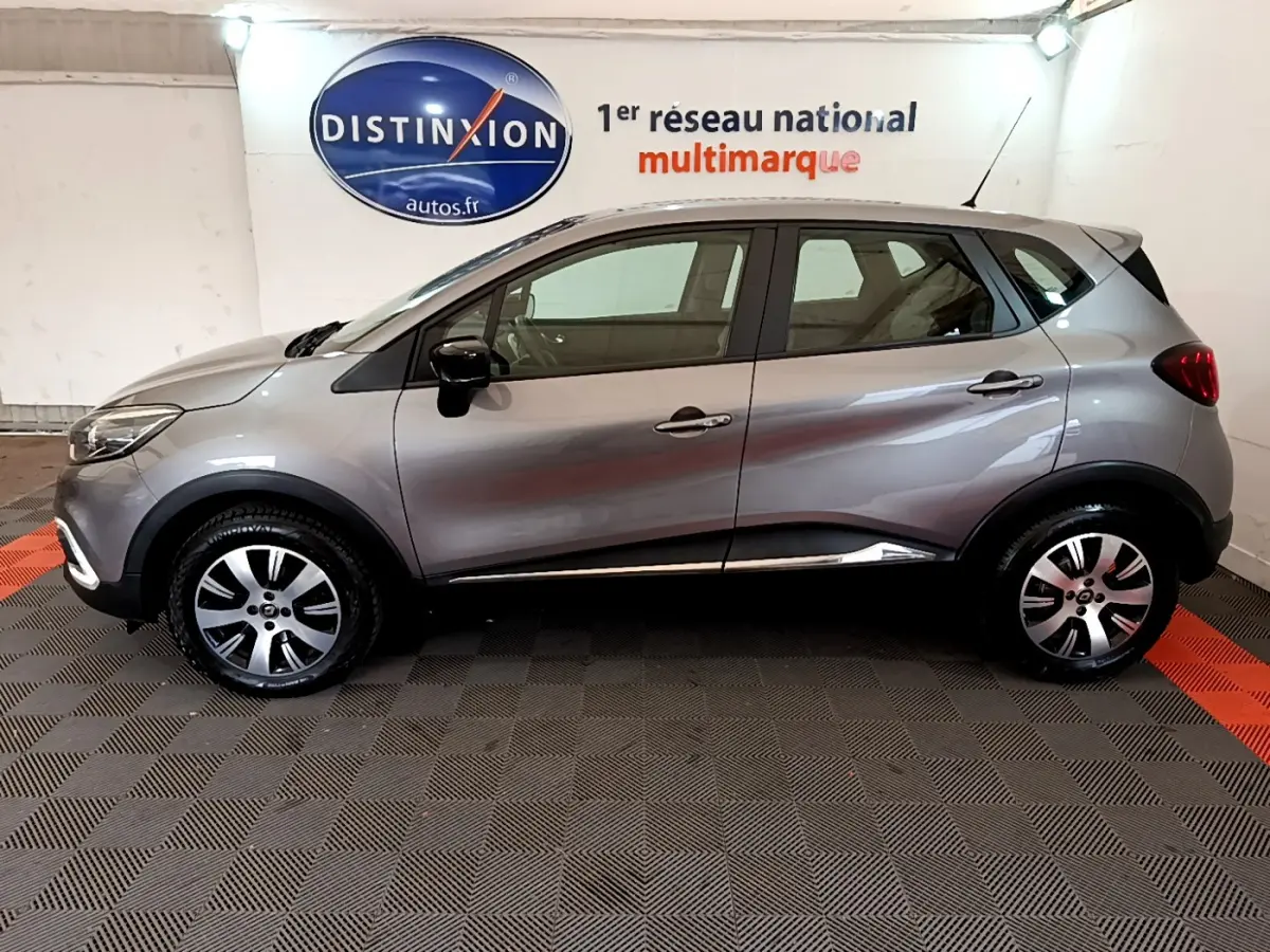 Profil côté gauche d'un Renault Captur Business gris foncé 2018 dans un showroom avec logo Distinxion en arrière-plan.