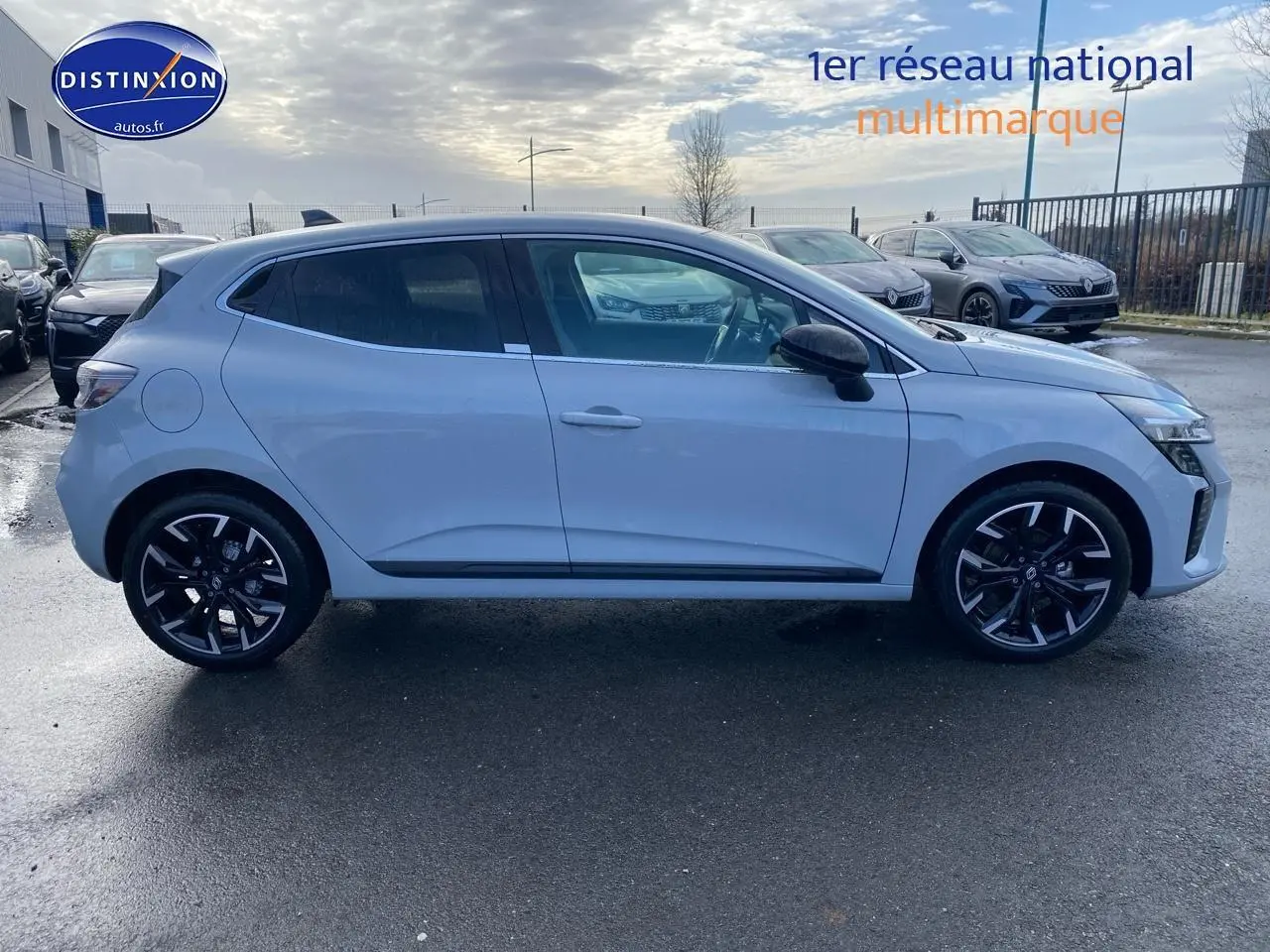 Profil droit d'une Renault Clio V gris rafale avec jantes alliage noires et rétroviseurs noirs, stationnée en extérieur.