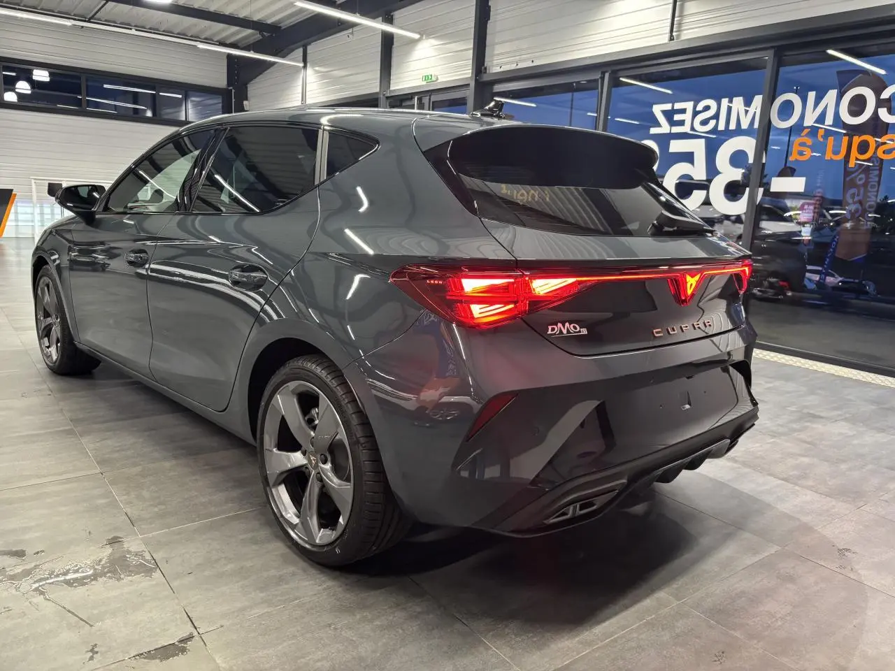 Vue 3/4 arrière droite de la CUPRA Leon 2026 en bleu Fjord avec feux arrière allumés et jantes alliage 18 pouces.