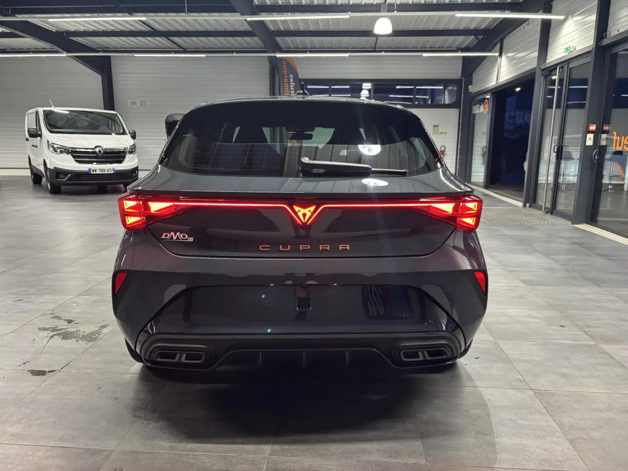 Vue arrière d'une CUPRA Leon bleu Fjord avec feux arrière Tri-LED et double sortie d'échappement noire en intérieur showroom.