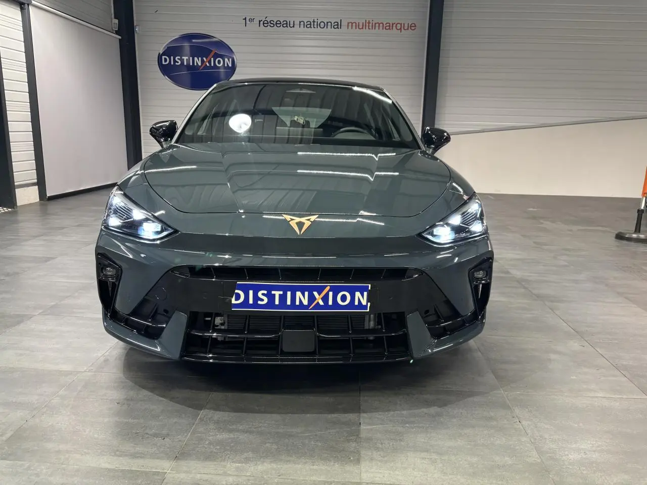 Vue frontale d'une CUPRA Leon bleu Fjord avec phares LED allumés et logo CUPRA cuivré sur le capot.