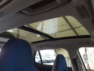 Vue intérieure du toit panoramique électrique d'un LYNK & CO 01 PHEV noir, avec sièges avant bleus visibles.