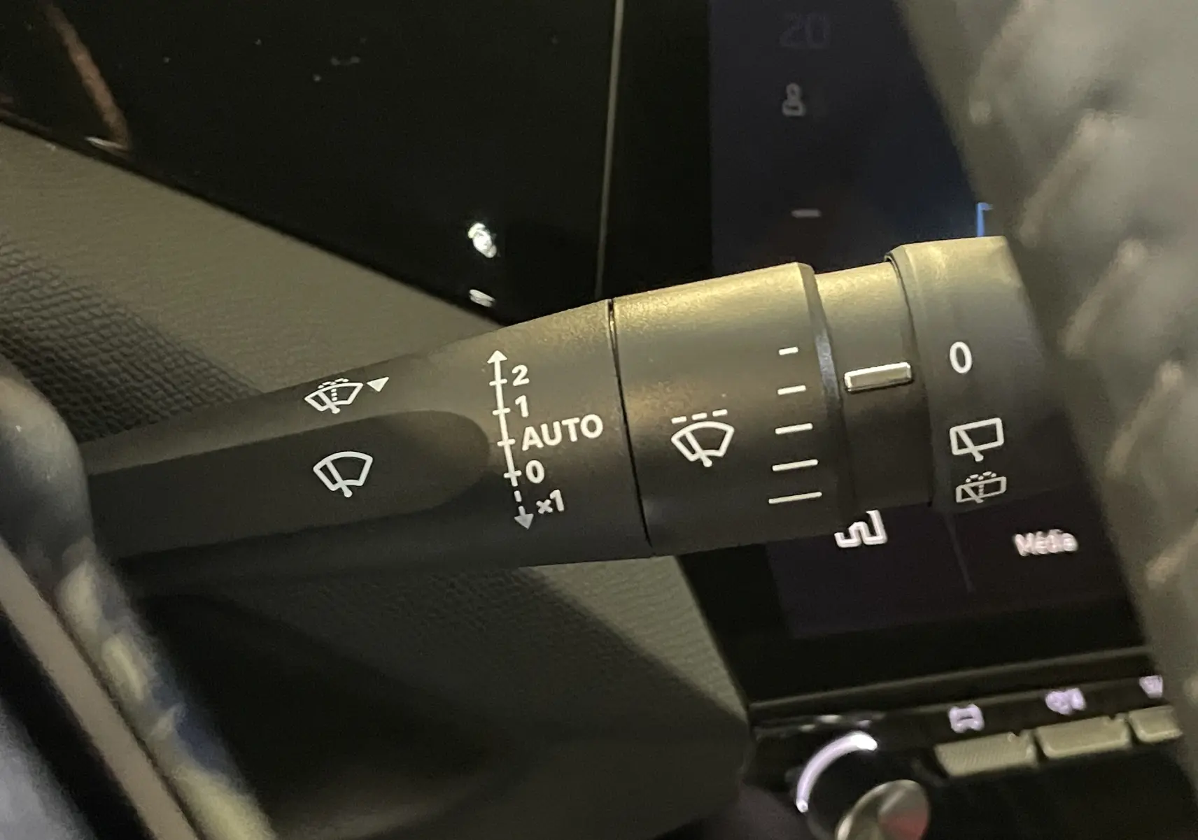 Gros plan sur la commande d’essuie-glace à gauche du volant dans l’habitacle sombre d’une Peugeot 308 Hybrid 2025.